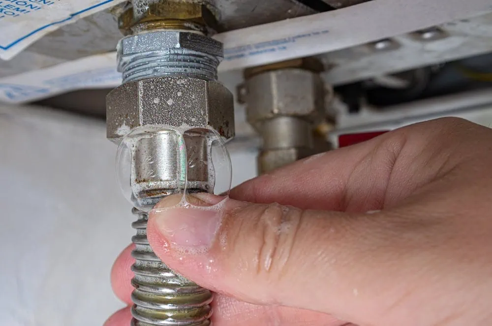 A hand pointing at a soapy bubble on a leaking pipe connection.