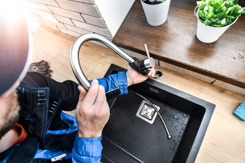A plumber's hands installing a modern kitchen faucet into a black sink.