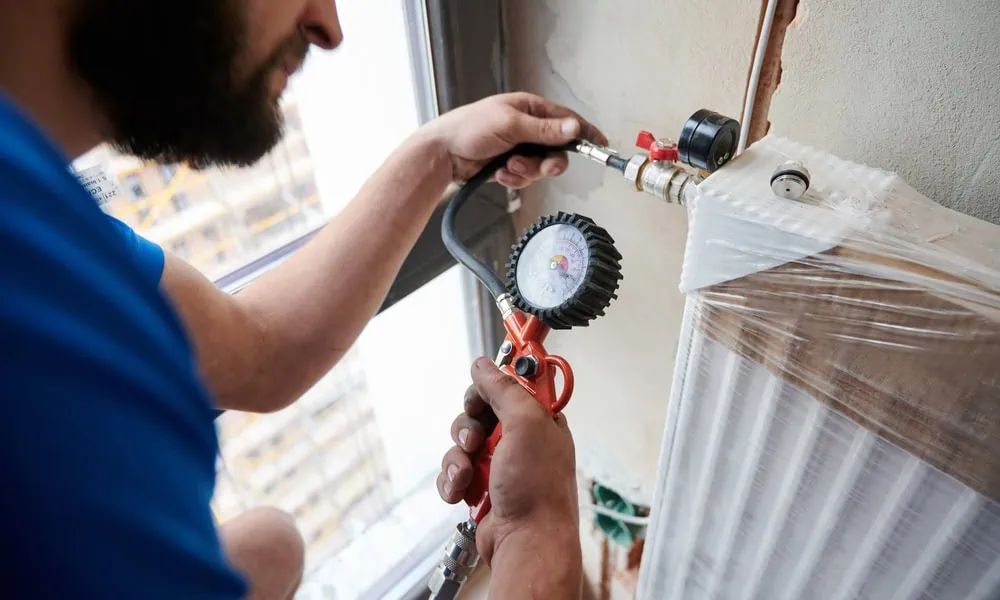A plumber uses a pressure gauge to check the pressure of a heating radiator.