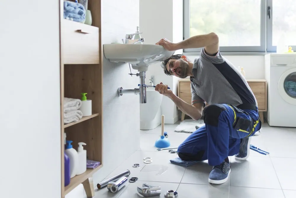 A plumber works on a sink in a bathroom.