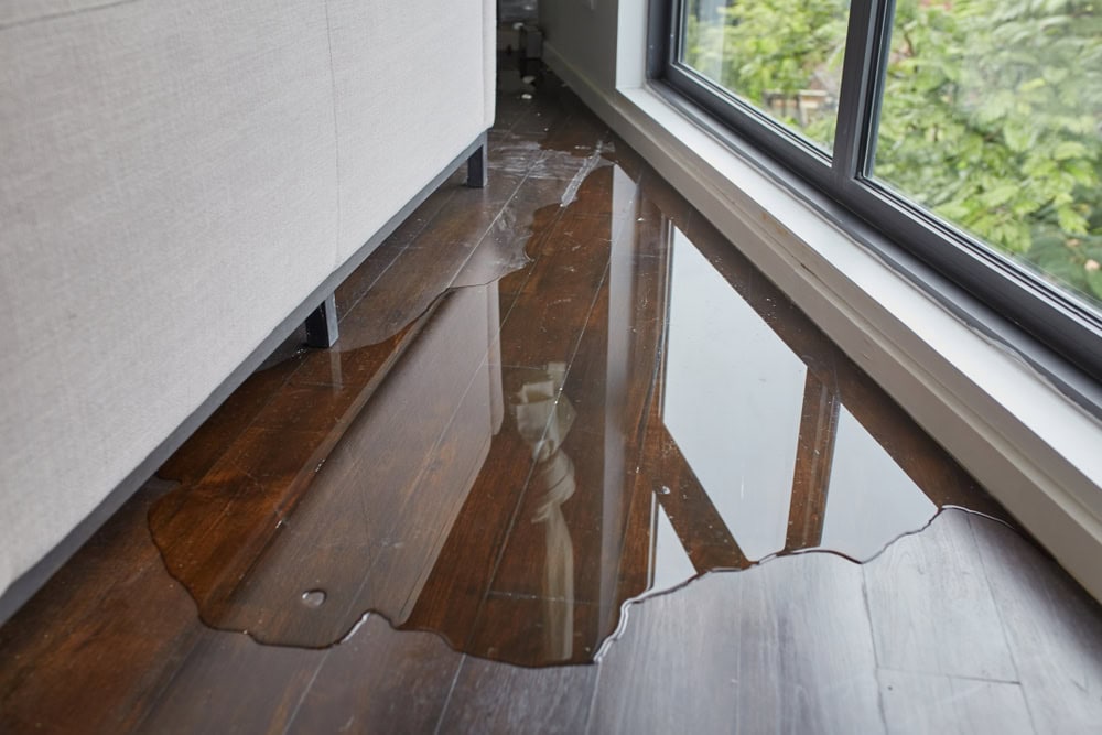 A large puddle of water on a shiny wooden floor in a modern room, indicating a water leak or flood.