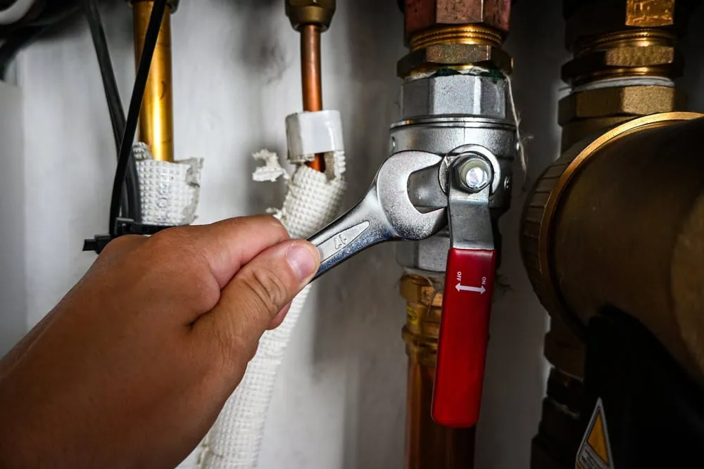 A hand uses a wrench to tighten a valve on a complex system of copper and brass pipes.